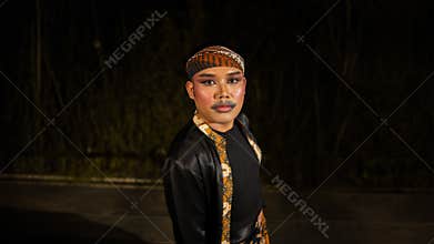 an Indonesian man dances with determination and skill while wearing a black costume on stage