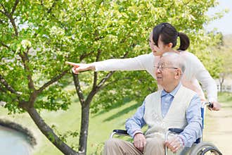 Asian senior man sitting on a wheelchair with caregiver pointing
