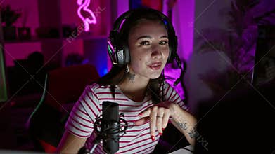 Young brunette woman with headphones podcasting in a neon-lit gaming room at night