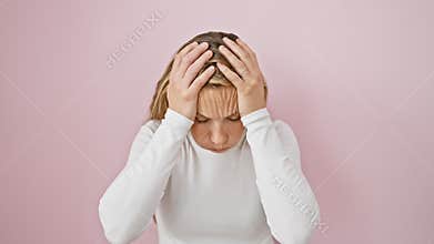 Aching blonde young woman, stressed and suffering from headache and migraine pain, stands isolated over pink background, hand on