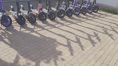 Row of electric scooters parked on sunny sidewalk casting long shadows indicating urban mobility and eco-friendly