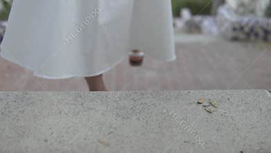 A woman in a white dress and sandals walks on the sidewalk