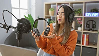 A young hispanic woman reviews headphones in a radio studio interior, portraying technology and podcasting