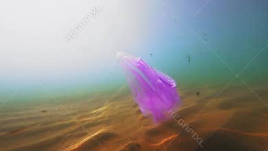 Plastic pollution, red purple plastic bag in blue water. Slow motion, discarded plastic bag drifts slowly under the
