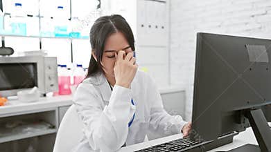 Exhausted and frustrated, young chinese female scientist at the lab rubs tired eyes and aching head amid stressful work