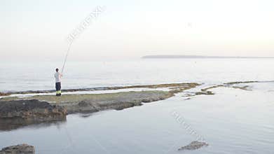 Man fishing in sea on rocky shore with water, sky, wind