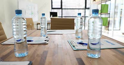 Bottles of water stand on wooden board table near clipboards