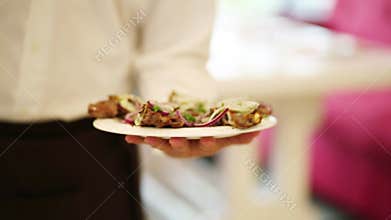 Waiter keeps and carries a plate with meat dish in