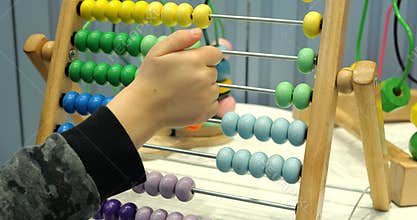 Toddler child counts on toy abacus in preschool classroom