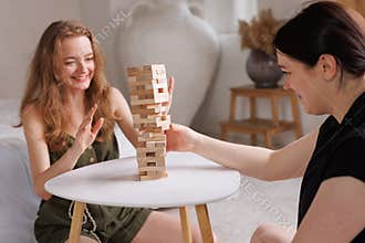 two women playing Jenga board game at home, excitement and relaxation, mind development concept,