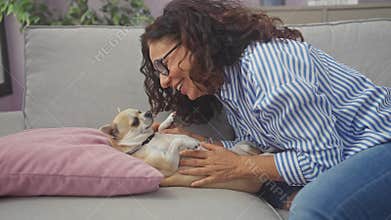 A middle-aged hispanic woman affectionately cuddling her pet chihuahua on a couch indoors