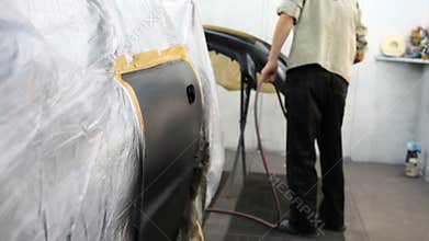Man paints car bumper in paint booth at service