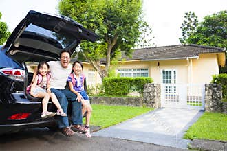 Family sitting in the car and their house behind