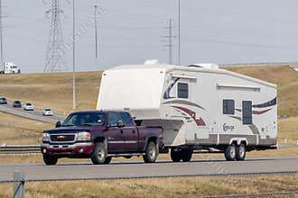 A maroon GMC Sierra HD truck towing a white fifth-wheel RV labeled \"Cruiser\" on a multi-