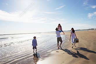 Rear View Of Family Walking Along Beach With Picnic Basket