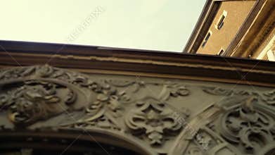 A low-angle shot of a building with elaborate stone carvings. The camera moves upwards, revealing the intricate details of the bu