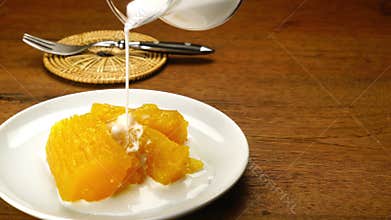 Pouring coconut milk over cassava in syrup.