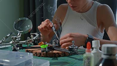 Woman assembling drone with magnifying glass and tools in home workshop
