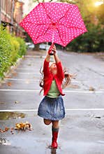Child with polka dots umbrella wearing red rain boots