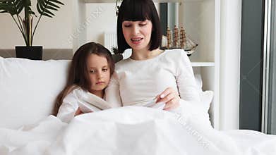 Mother reading book to daughter in cozy bedroom