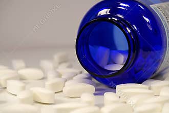 Big white pills scattered on the table. Overdose. Open blue container