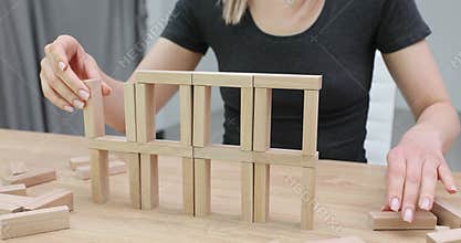 Woman builds wooden structure from blocks on table
