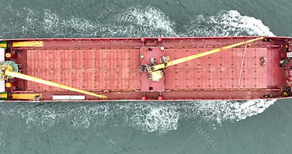 Aerial top down view of a red cargo ship sailing in open sea.