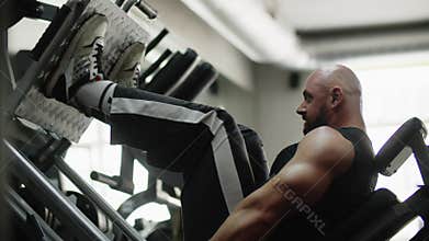 Man bodybuilder sideways in the gym training on the machine concentratedly. Exercise for leg strength and endurance. The