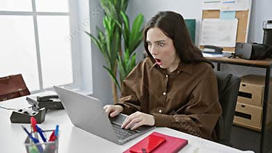 A surprised young woman working on her laptop in a modern office room, reflecting a professional, indoor scenario