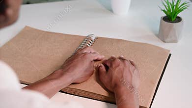 people with vision problems, black man reads braille book and runs his fingers along page while sitting at table in room