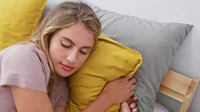 Attractive young blonde woman, exhausted yet comfortable, snuggles under a cozy blanket, lying in her warm bed, ready to drift