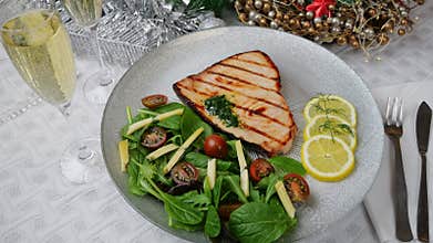 Grilled swordfish steak with fresh salad, tomatoes and cheese on a plate rotating. Christmas New Year decoration.
