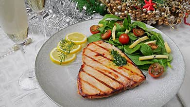 Grilled swordfish steak with fresh salad, tomatoes and cheese on a plate rotating. Christmas New Year decoration.