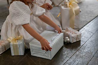 A young girl is opening a gift box with a ribbon on it. The scene is set in a room with a few other gift boxes and a