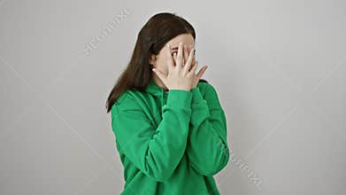 Peekaboo! young woman, clad in sweatshirt on white, her eyes wide with shock, covers blushing face with shy hand peek, expression