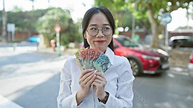 Smiling asian woman in glasses holds australian currency in city street