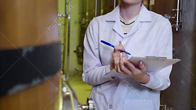 Winemaker woman checking and examining producing wine at winery in factory.