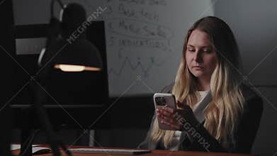 A young woman is using a smartphone in an office environment against a background of data analysis