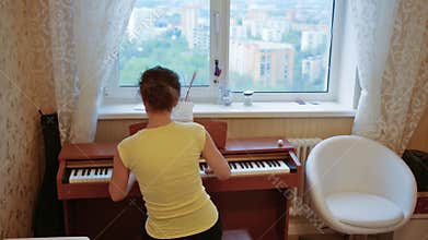 Young woman in T-shirt is playing on the piano