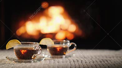 Two cups of hot tea with lemon on a table against the background of the fireplace