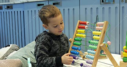 Smart toddler boy counts on wooden abacus in kindergarten