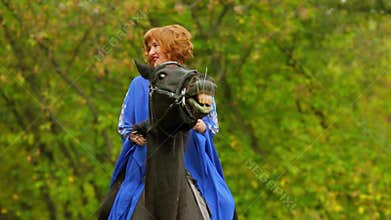 Red haired woman in blue cloak sits on chestnut