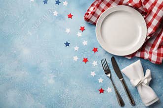 Top view to festive table with white empty plate, tablecloth, red, white, blue stars confetti on blue background. USA