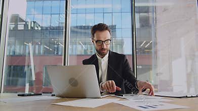 Concentrated businessman trader are tired. The man takes off his glasses and rubs his tired eyes. Sits at laptop