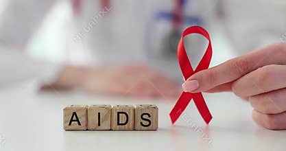 Doctor holds red ribbon near cubes with word AIDS on table