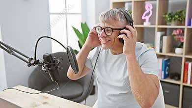Smiling senior man podcasting with microphone and headphones in a home studio setting