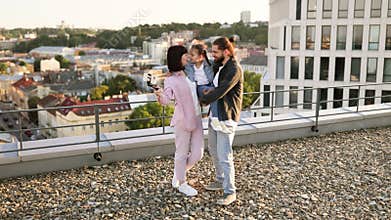 Happy family taking selfie on urban rooftop during sunset