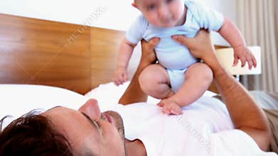 Happy father lying with baby son bouncing on his chest