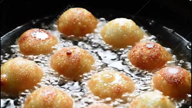 Golden fried dough ball dessert simmering in dark syrup on a frying pan