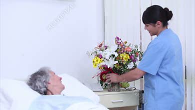 Serene senior woman speaking at a nurse who gives a bouquet of flowers